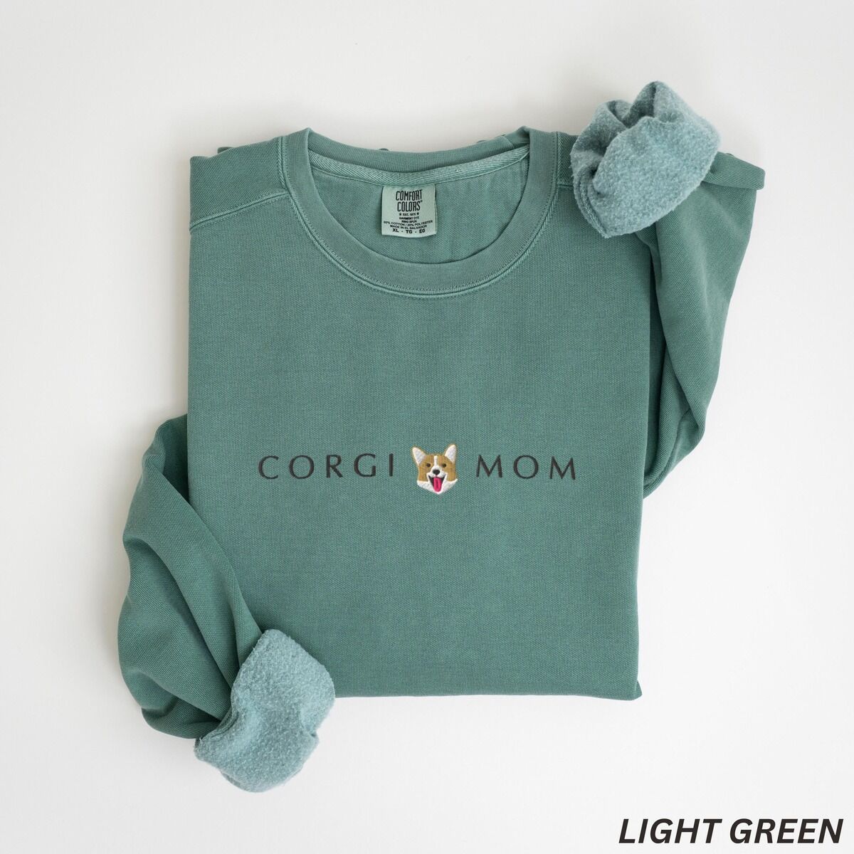 Corgi Mom Sweatshirt – Light Green Light Green crewneck sweatshirt laid flat on white, embroidered with CORGI MOM and a corgi face with a pink tongue