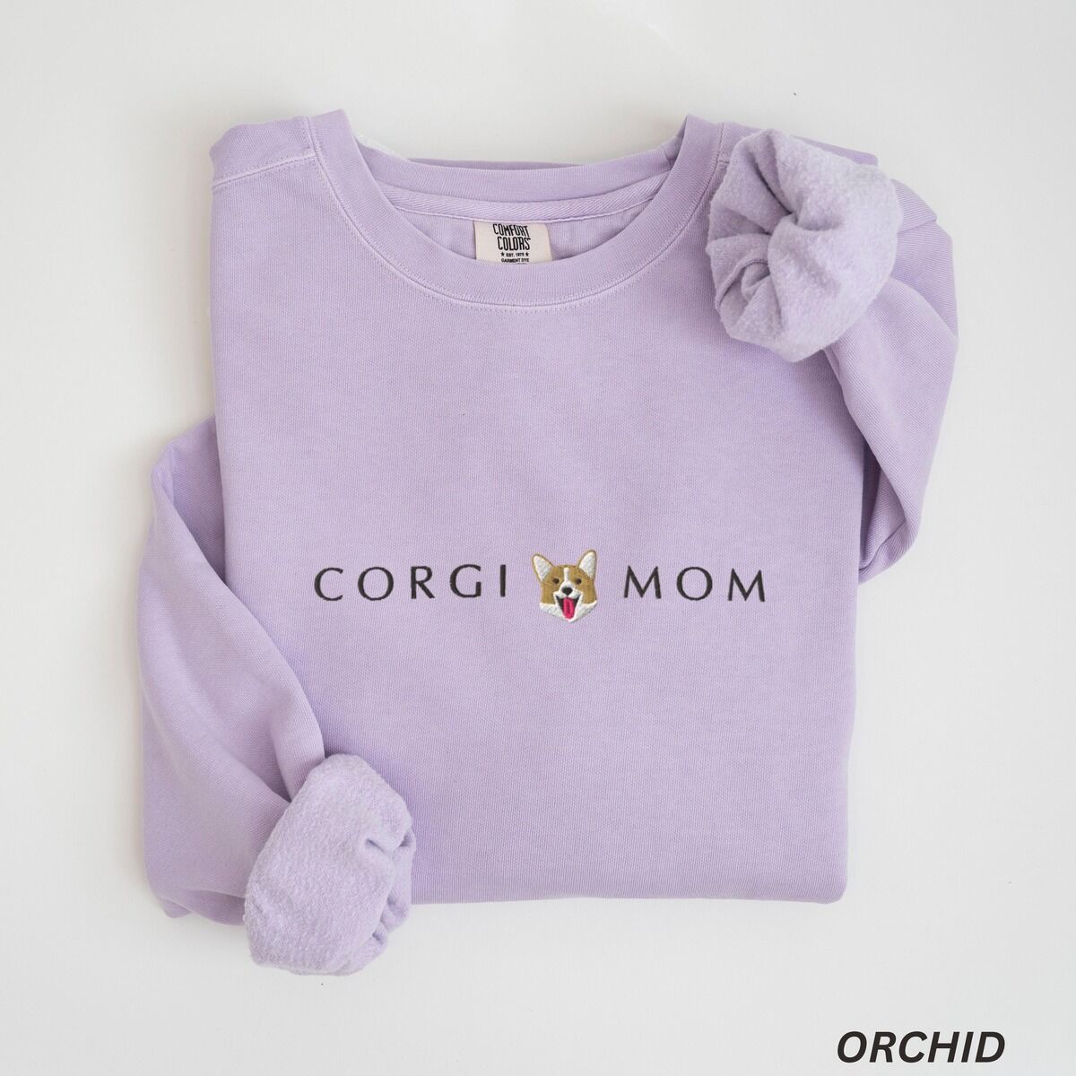 Corgi Mom Sweatshirt – Orchid Orchid crewneck sweatshirt laid flat on white, embroidered with CORGI MOM and a small smiling Pembroke corgi face