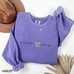Violet crewneck sweatshirt laid flat with a felt hat and dried palm leaves, embroidered with CORGI MOM and a smiling corgi face