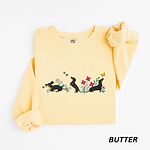Butter crewneck sweatshirt laid flat on white, embroidered with three black and tan dachshunds playing among white daisies and pink spring flowers, with two bees and a yellow butterfly, across the chest