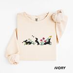 Ivory crewneck sweatshirt laid flat on white, embroidered with three black and tan dachshunds playing among white daisies and pink spring flowers, with two bees and a yellow butterfly, across the chest