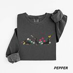 Pepper crewneck sweatshirt laid flat on white, embroidered with three black and tan dachshunds playing among white daisies and pink spring flowers, with two bees and a yellow butterfly, across the chest