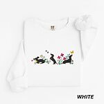 White crewneck sweatshirt laid flat on white, embroidered with three black and tan dachshunds playing among white daisies and pink spring flowers, with two bees and a yellow butterfly, across the chest