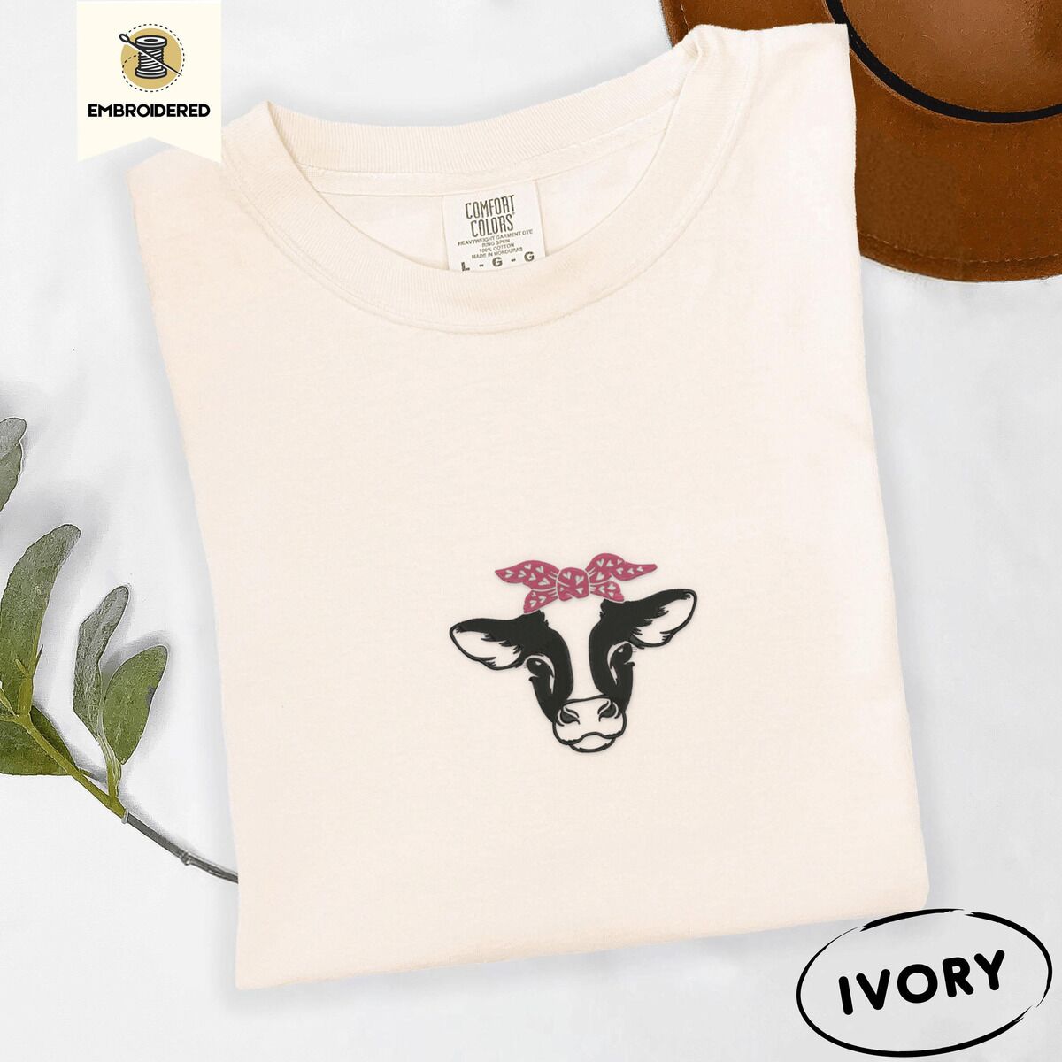 Cow Bandana Shirt – Ivory Ivory Comfort Colors T-shirt embroidered with a black and white cow head wearing a pink heart bandana tied in a bow