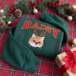 Forest green custom cat Christmas sweatshirt with a reindeer cat portrait and varsity name on a plaid tablecloth