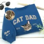 Custom cat dad sweatshirt in royal blue with CAT DAD varsity letters, an embroidered tabby kitten portrait, EST. 2024 and the name Neko with a fish bone on the sleeve