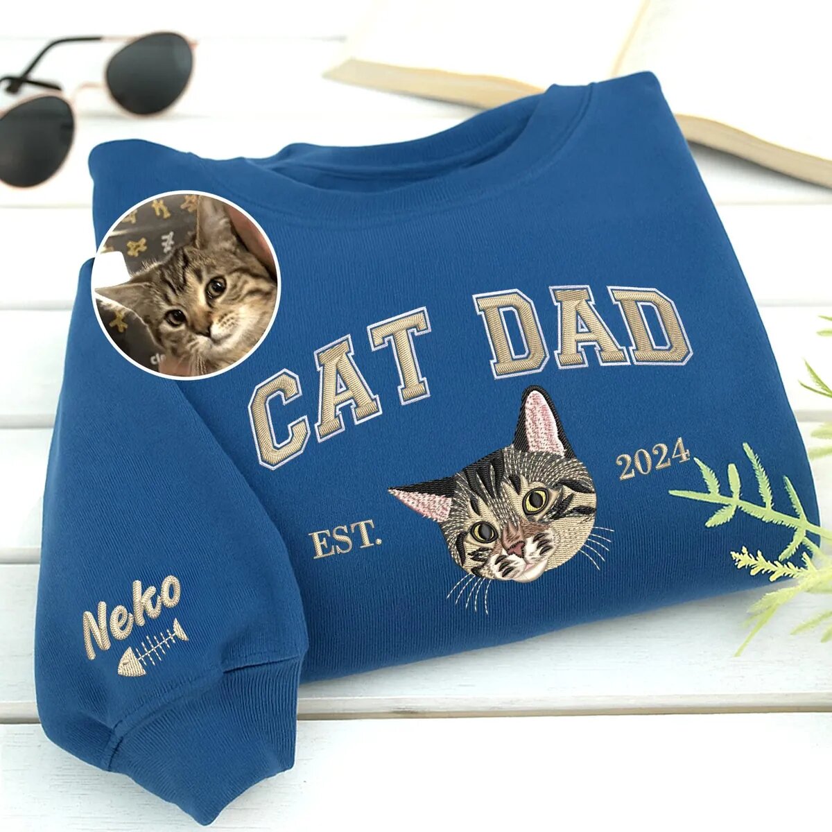 Custom Cat Dad Sweatshirt – Royal Blue Custom cat dad sweatshirt in royal blue with CAT DAD varsity letters, an embroidered tabby kitten portrait, EST. 2024 and the name Neko with a fish bone on the sleeve