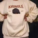 Cream crewneck with an embroidered black dog face, the name KRINGLE and EST 2022