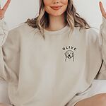 Woman making peace signs in a Sand crewneck sweatshirt embroidered with a line art golden retriever face and the name OLIVE