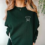 Woman in a Forest Green crewneck sweatshirt embroidered in white with a line art golden retriever face and the name OLIVE