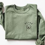 Military Green crewneck sweatshirt laid flat, embroidered with a line art golden retriever face and the name OLIVE on the left chest