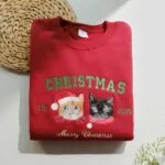 Custom pet Christmas sweatshirt in red with two embroidered cat portraits in Santa hats, green CHRISTMAS letters, EST 2025 and Merry Christmas script