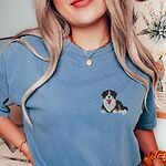Woman in a Blue Jean T-shirt embroidered with a small tricolor Berner puppy lying down on the left chest
