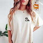 Woman in an Ivory T-shirt embroidered with a small Berner puppy lying down with its tongue out on the left chest