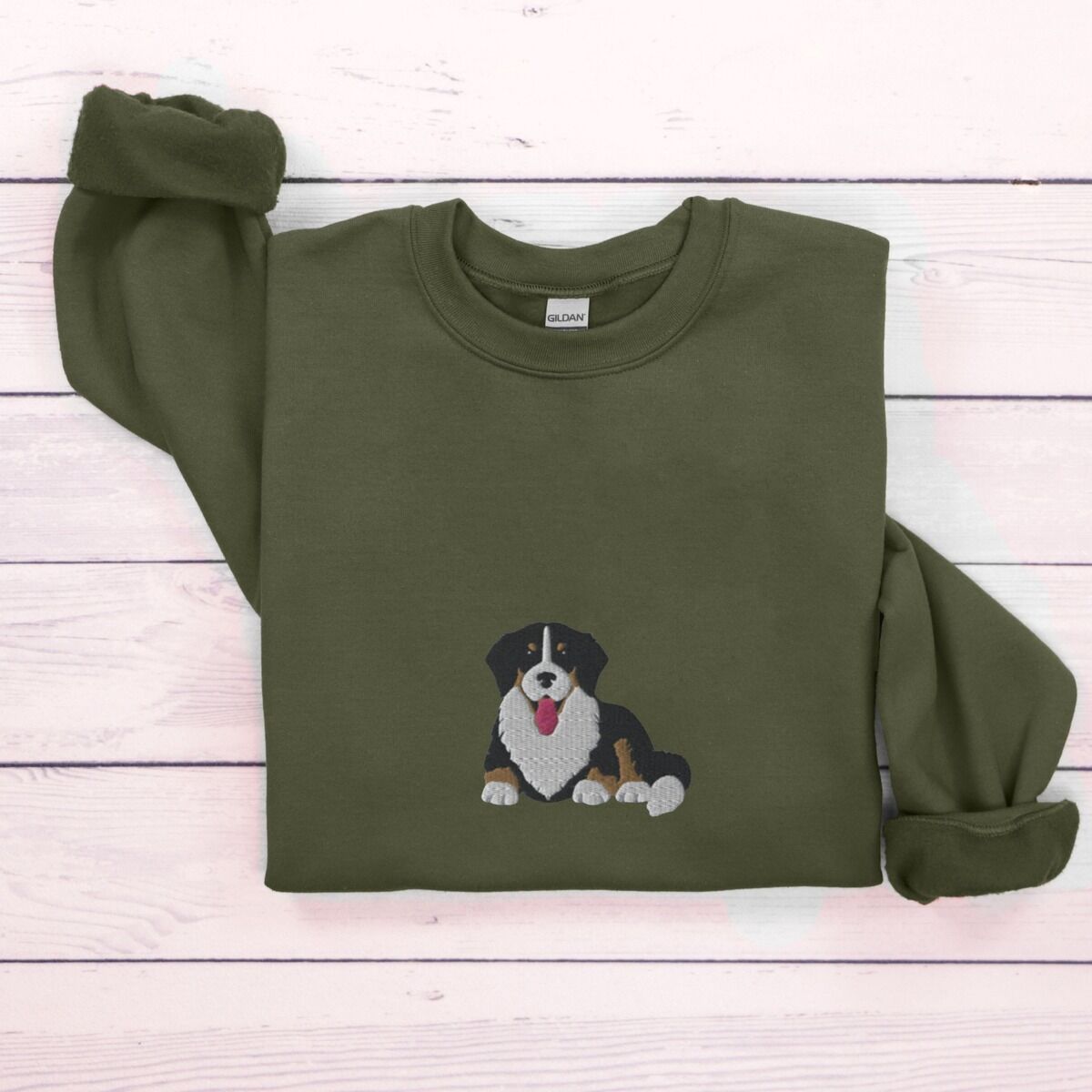 Cute Bernese Mountain Dog Sweatshirt - center chest in green Military Green crewneck sweatshirt laid flat on whitewashed wood, embroidered with a larger tricolor Berner puppy in the center of the chest
