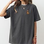 Woman in a Pepper T-shirt embroidered with a cartoon golden retriever in a Santa hat tangled in colored lights on the left chest