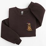 Dark Chocolate crewneck sweatshirt laid flat, embroidered with a smiling cartoon golden retriever in a Santa hat tangled in colored lights