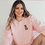 Smiling woman in a Light Pink crewneck sweatshirt embroidered with a cartoon golden retriever wrapped in Christmas lights