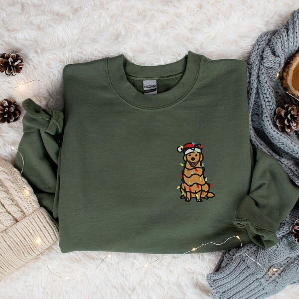 Cute golden retriever Christmas sweatshirt in Military Green on a faux fur throw with pinecones, embroidered with a cartoon golden in a Santa hat tangled in Christmas lights
