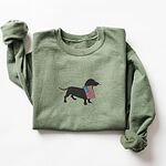 Military Green crewneck sweatshirt laid flat, embroidered with a black dachshund carrying a stars-and-stripes flag
