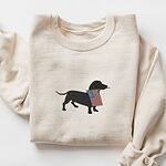 Sand crewneck sweatshirt laid flat with a rolled sleeve, embroidered with a dachshund silhouette carrying a USA flag