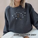 Woman sitting in a Dark Heather crewneck sweatshirt, embroidered with a dachshund standing up on its hind legs with its nose to the sky among falling snowflakes