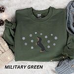 Military Green crewneck sweatshirt laid flat on a fur rug beside a knit hat and pinecones, embroidered with a dachshund standing up on its hind legs with its nose to the sky among falling snowflakes