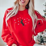 Woman by a Christmas tree in a Red crewneck sweatshirt, embroidered with a dachshund standing up on its hind legs with its nose to the sky among falling snowflakes