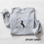 Sport Grey crewneck sweatshirt folded on a white background, embroidered with a dachshund standing up on its hind legs with its nose to the sky among falling snowflakes