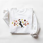 White crewneck sweatshirt laid flat on white, embroidered with a black and tan dachshund sitting up on its hind legs among orange, red and gold autumn leaves across the chest