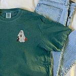 Blue Spruce T-shirt laid on a bed beside folded jeans, embroidered on the left chest with a ghost sipping iced coffee, a black and tan dachshund and a jack-o'-lantern pail