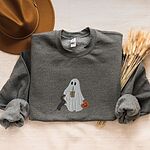Dark Heather crewneck sweatshirt laid flat with a brown hat and wheat stems, embroidered with a ghost sipping iced coffee, a black and tan dachshund standing up at her side and a jack-o'-lantern pail