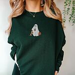 Woman in a Forest Green crewneck sweatshirt embroidered with a ghost sipping iced coffee, a red dachshund standing up at her side and a jack-o'-lantern pail
