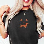 Woman in a Black T-shirt embroidered across the chest with an orange dachshund jack-o'-lantern face