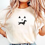 Woman in an Ivory T-shirt embroidered across the chest with a black jack-o'-lantern face whose grin is a dachshund silhouette