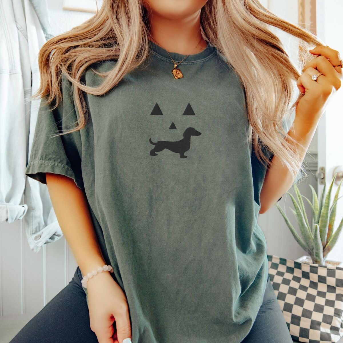 Dachshund Jack-o'-Lantern Shirt – Moss Woman in a Moss T-shirt embroidered across the chest with a black jack-o'-lantern face with a dachshund silhouette smile