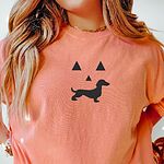 Woman in a Terracotta T-shirt embroidered across the chest with a black dachshund jack-o'-lantern face