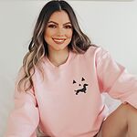 Woman smiling in a Light Pink crewneck sweatshirt embroidered on the left chest with a black dachshund jack-o'-lantern face