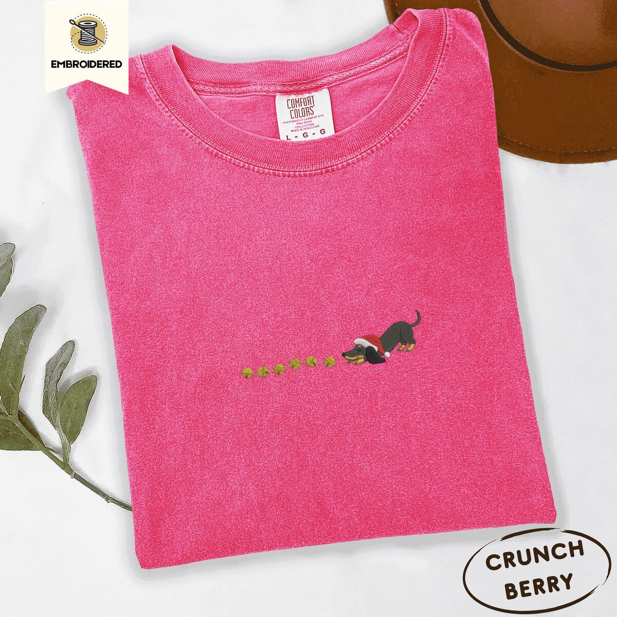 Dachshund Jingle Bells Shirt – Crunchberry Crunchberry Comfort Colors T-shirt embroidered with a black and tan dachshund in a Santa hat bowing down to sniff a string of gold jingle bells