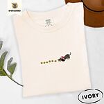 Ivory Comfort Colors T-shirt embroidered with a black and tan dachshund in a Santa hat bowing down to sniff a string of gold jingle bells