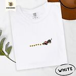 White Comfort Colors T-shirt embroidered with a black and tan dachshund in a Santa hat bowing down to sniff a string of gold jingle bells