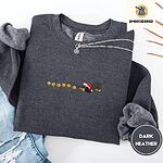 Dark Heather crewneck sweatshirt folded with ripped jeans and a silver chain necklace, embroidered with a black and tan dachshund in a Santa hat bowing down to sniff a string of six gold jingle bells