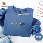 Indigo Blue crewneck sweatshirt folded with light jeans and dried twigs, embroidered with a black and tan dachshund in a Santa hat bowing down to sniff a string of six gold jingle bells
