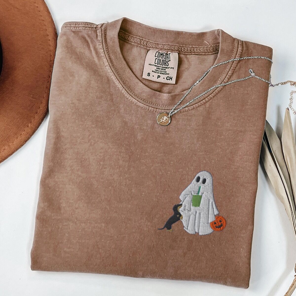 Dachshund Matcha Shirt – Espresso Espresso T-shirt folded flat with a necklace, a brown hat and dried palm leaves, embroidered with a ghost sipping an iced matcha, a black and tan dachshund at her side and a jack-o'-lantern pail on the left chest