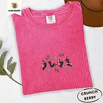 Crunchberry Comfort Colors T-shirt embroidered with four black and tan dachshunds in Santa hats leaping between sprigs of mistletoe and silver snowflakes
