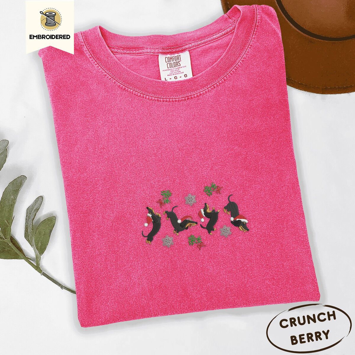 Dachshund Mistletoe Shirt – Crunchberry Crunchberry Comfort Colors T-shirt embroidered with four black and tan dachshunds in Santa hats leaping between sprigs of mistletoe and silver snowflakes