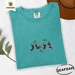Seafoam Comfort Colors T-shirt embroidered with four black and tan dachshunds in Santa hats leaping between sprigs of mistletoe and silver snowflakes