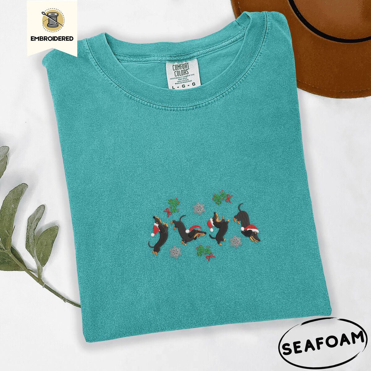 Dachshund Mistletoe Shirt – Seafoam Seafoam Comfort Colors T-shirt embroidered with four black and tan dachshunds in Santa hats leaping between sprigs of mistletoe and silver snowflakes