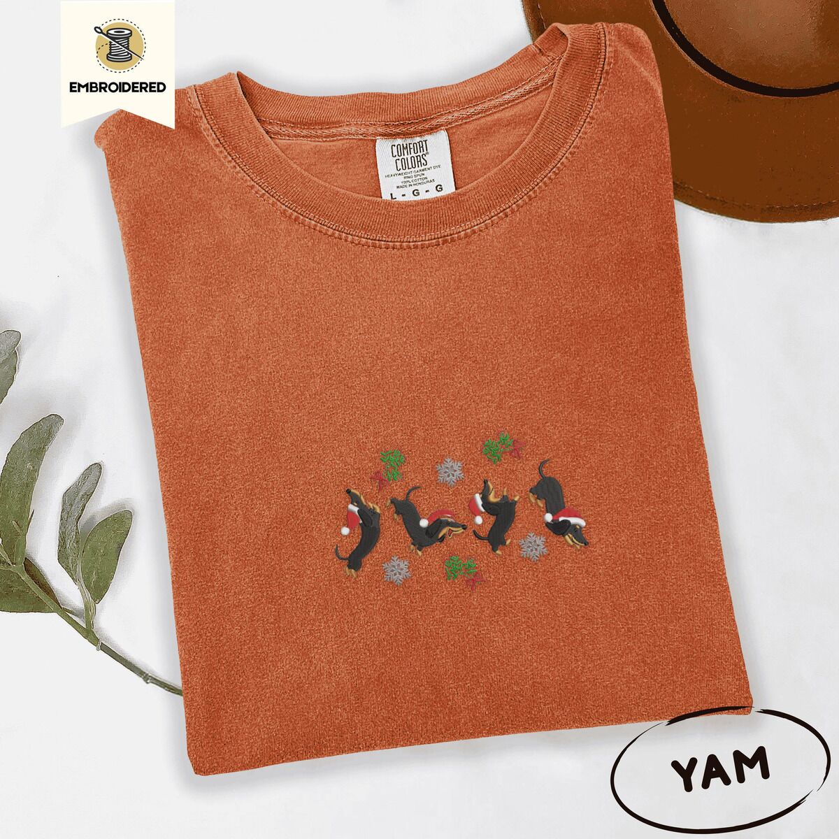 Dachshund Mistletoe Shirt – Yam Yam Comfort Colors T-shirt embroidered with four black and tan dachshunds in Santa hats leaping between sprigs of mistletoe and silver snowflakes