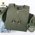 Military Green crewneck sweatshirt folded with light jeans and a silver chain necklace, embroidered with four black and tan dachshunds in Santa hats leaping between mistletoe sprigs with red bows and silver snowflakes